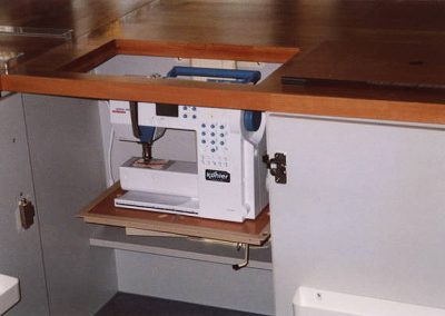 Eine Nähmaschine wird durch die geöffnete Tischplatte herausgehoben